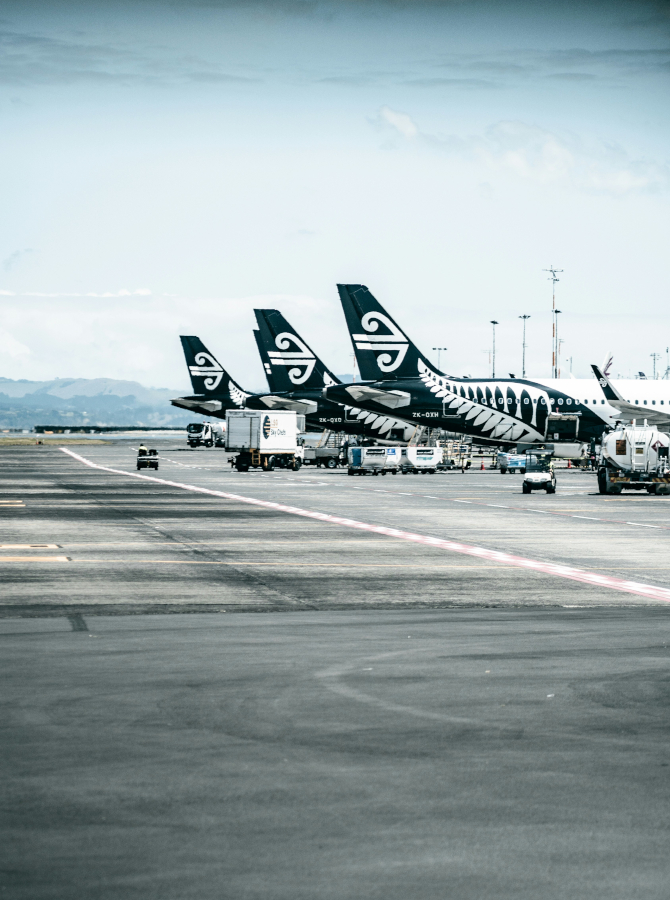 Air New Zealand aircraft parked on an airport tarmac with ground service vehicles alongside.